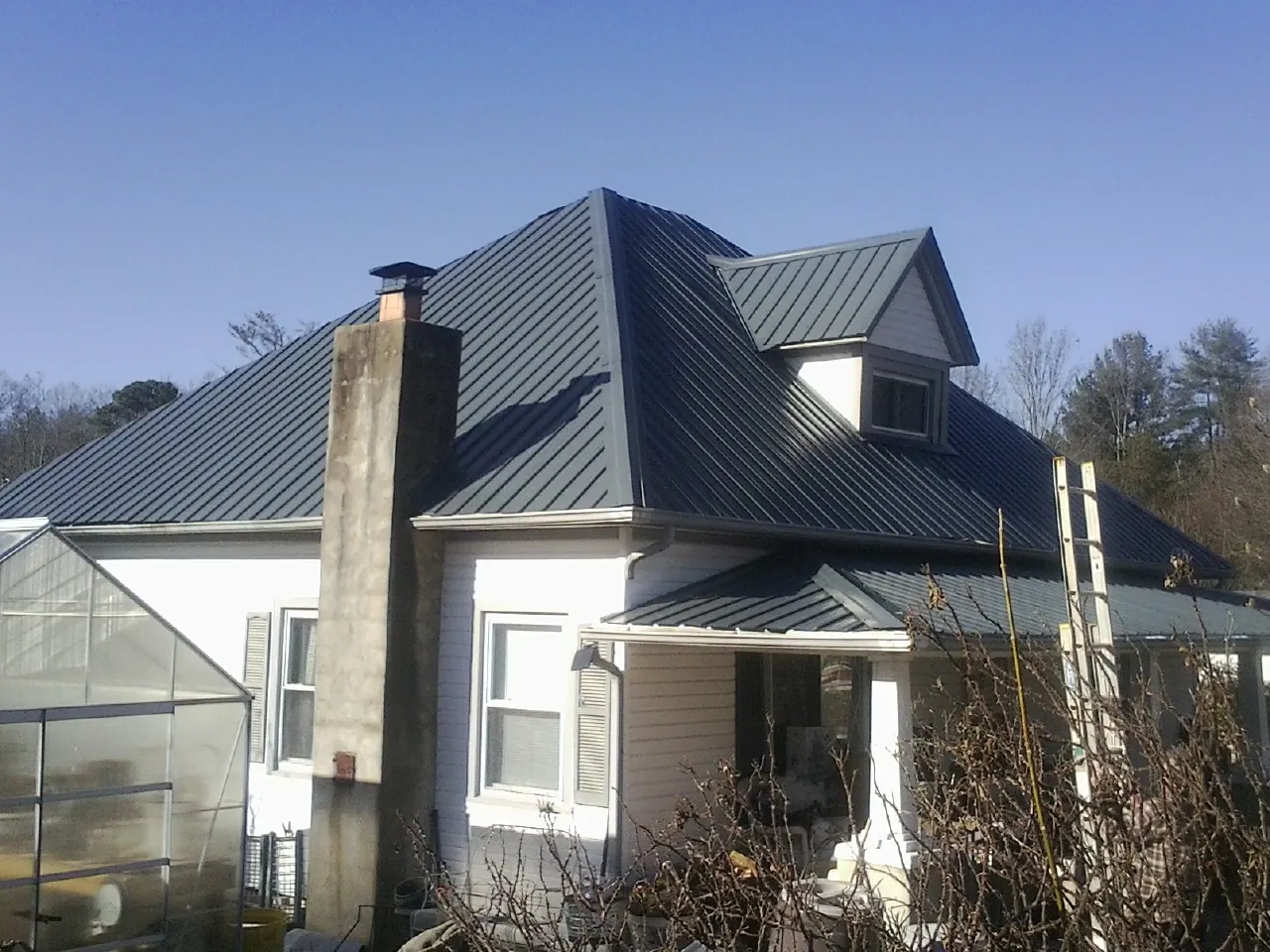Dark blue standing seam metal roof on a white farmhouse with dormer — Slate & Tile Roof Repair by Roofing Brothers in Callaway