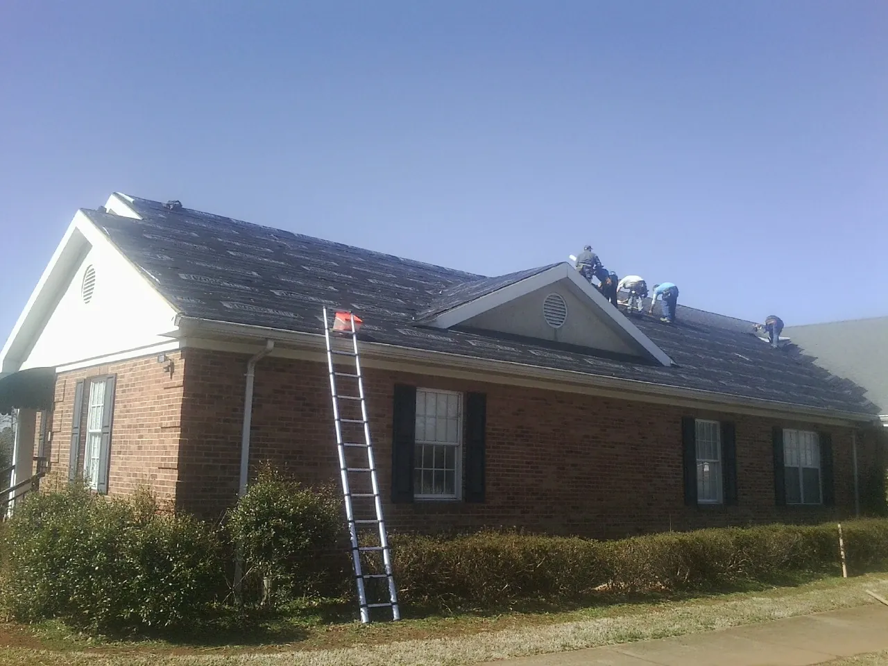 Crew tearing shingles off a brick ranch roof with a ladder set — Emergency Roof Repair work by our crew in Callaway