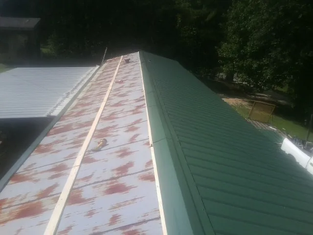 Old rusted panels beside newly installed green metal roofing — Wind Damage Roof Repair by Roofing Brothers in Callaway