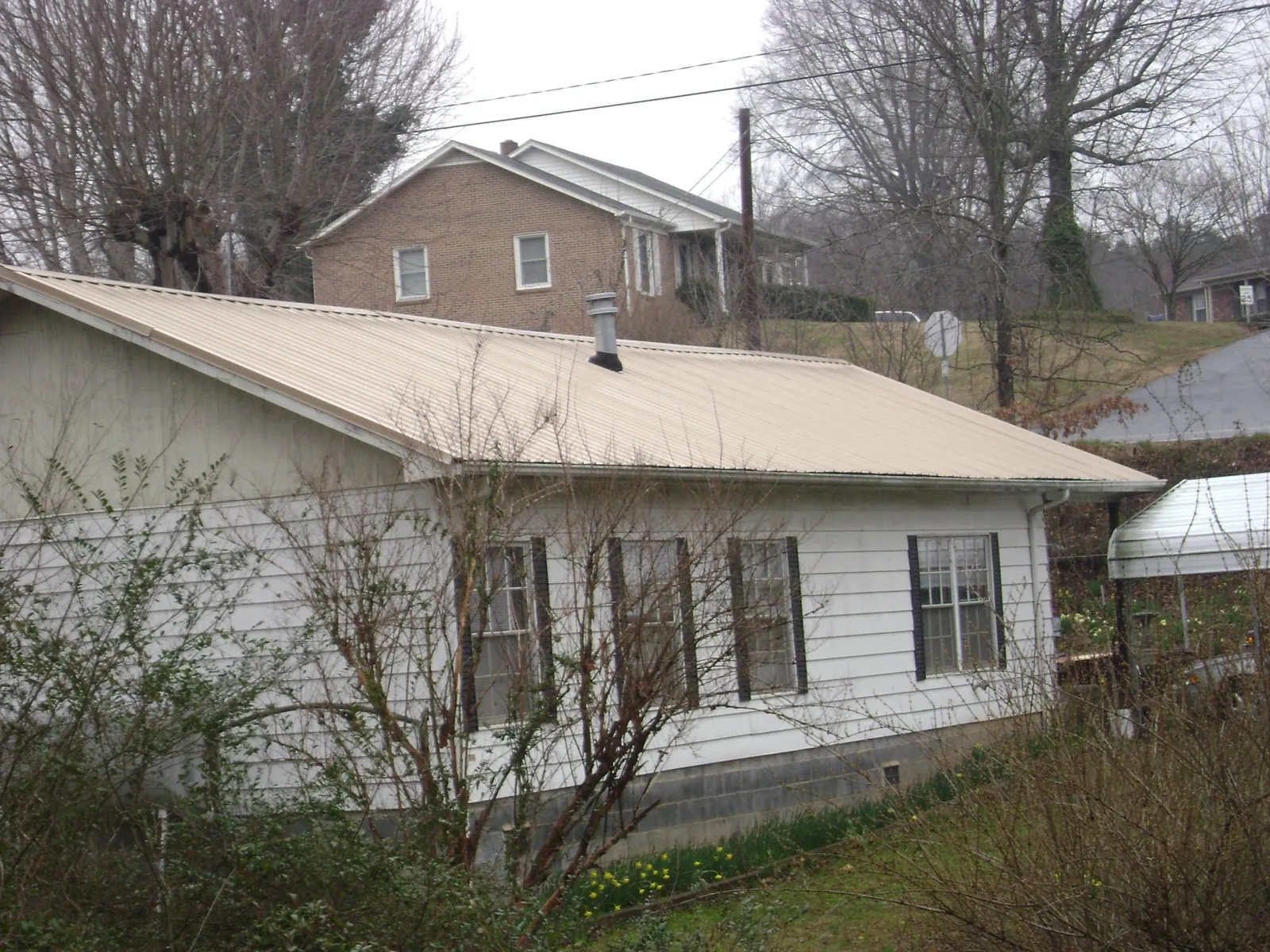 Tan metal roof on a white sided house set into a hillside — Commercial Roofing by Roofing Brothers in Callaway